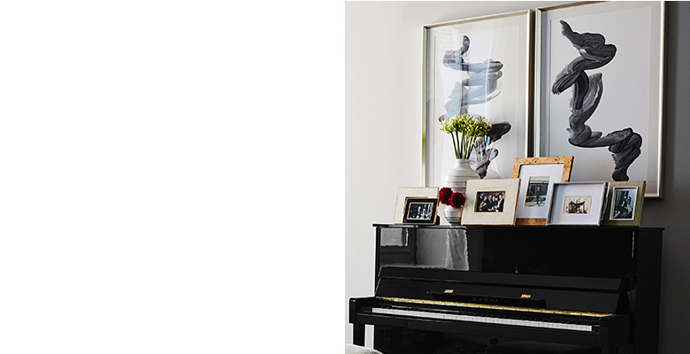 “It’s so important to incorporate what people love into their space,” says Lainey. To celebrate Jenny’s passion for playing the piano, Lainey created a focal wall around the piano. “The apartment has very high ceilings so we designed up above the piano in order to draw the eye in.” The framed photos make personal mementos prominent and the black abstract art echoes the color of the piano itself. “It’s so important to incorporate what people love into their space,” says Lainey. To celebrate Jenny’s passion for playing the piano, Lainey created a focal wall around the piano. “The apartment has very high ceilings so we designed up above the piano in order to draw the eye in.” The framed photos make personal mementos prominent and the black abstract art echoes the color of the piano itself.
